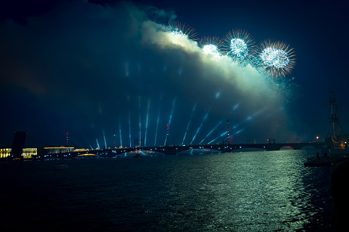 Beautiful green and blue firework explodes in night city sky above bridge. Pyrotechnic display. Copy space for your text. Holiday celebration theme.