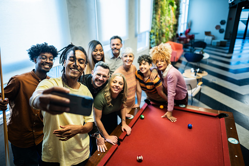 Coworkers taking a selfie and playing snooker after work at office