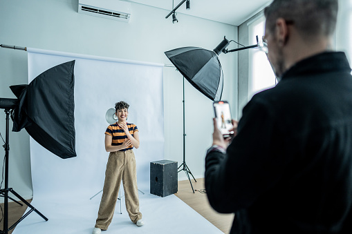 Photographer taking photos/filming a young model woman at studio