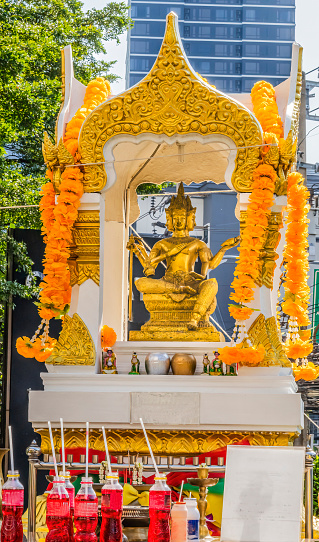 Golden Yellow Buddha Spirit House Shrine Marigold Garlands Red Soda Offerings Downtown Bangkok Thailand. Shrine to the protective guardian spirit of place