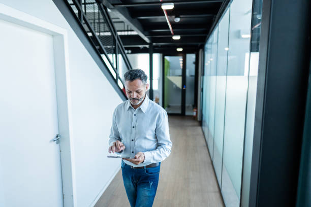 istock Mature businessman using digital tablet and walking at office 1621319457