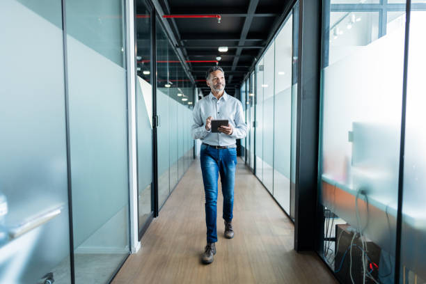 Mature businessman using digital tablet and walking at office