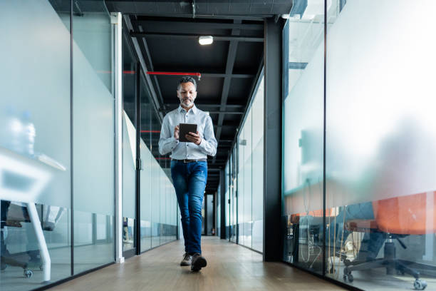 istock Mature businessman using digital tablet and walking at office 1621319468