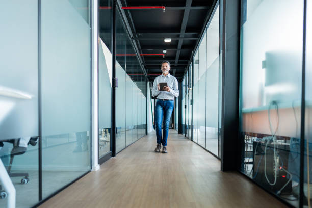 istock Mature businessman using digital tablet and walking at office 1621319469