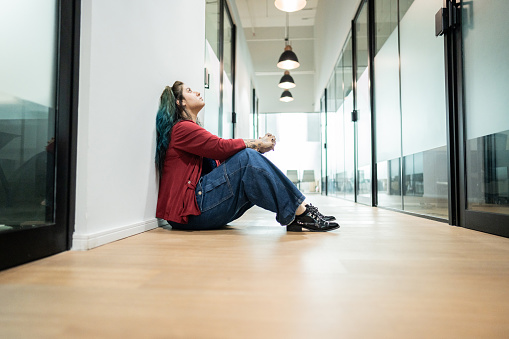 Worried businesswoman sitting on ground at office corridor