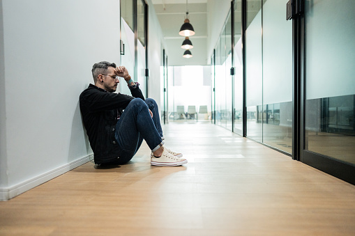 Worried businessman sitting on ground at office corridor