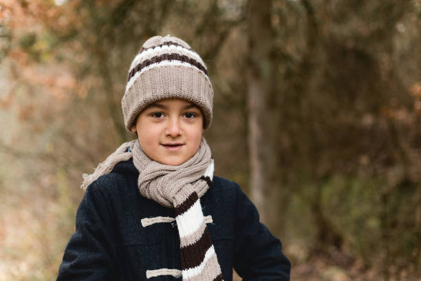 Young boy dressed in warm cloth standing in the forest and looking at camera
