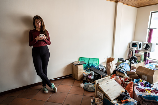 Young woman using mobile phone during house moving at the new apartment