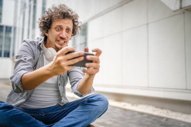 One caucasian man sit outdoor take a brake happy smile play video games leisure activity having fun hold mobile phone use smartphone have fun online copy space adult male