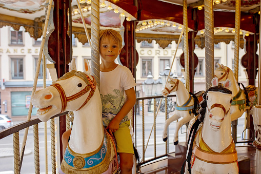 Children, boys, going on Merry Go Round, kids play on carousel summertime in Strasbourg, France during summer vacation