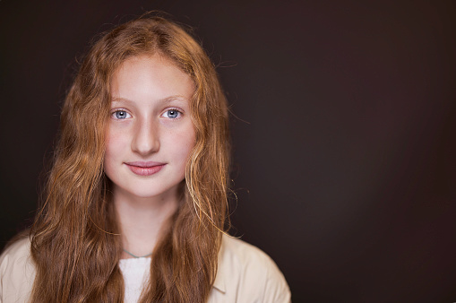 Pre-teen girl with long red gold hair and wearing a cream top.