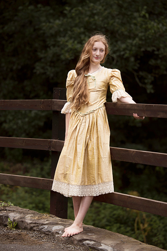 Pre-teen barefoot girl with long red/blond hair wearing a golden dress.