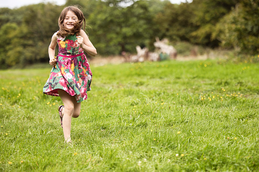 Primary age brunette, wearing a Summer dress, running in the park.