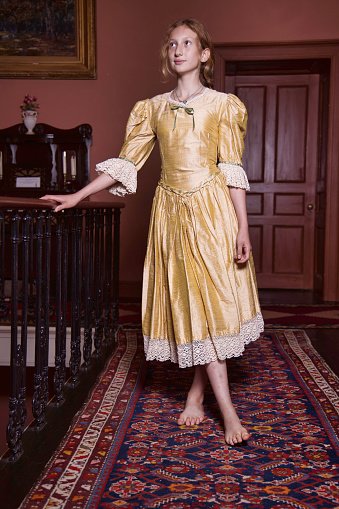 11-year-old blonde girl at home wearing a golden silk dress.