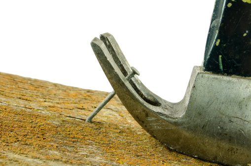 An fibreglass handeled  hammer pulling a nail from a barn board covered with lichen. On a white background. Close-up