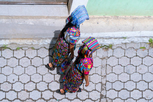 Three women dressed in cultural attire display their weaving skills on a village road in Ecuador.