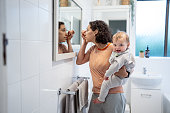 Mother holds her baby son as she applies makeup in bathroom