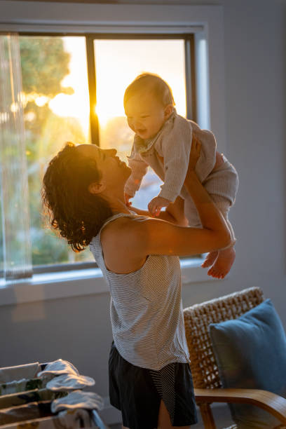 Loving mother smiles at baby son while playing together Adorable Eurasian 9 month old baby boy who is at home with his mom smiles as his mother playfully lifts him in the air while dancing together at sunset. baby boy dancing with his mommy stock pictures, royalty-free photos & images