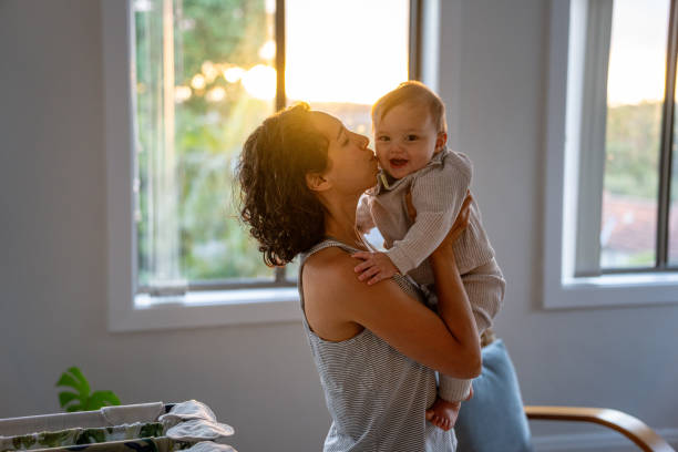 Loving mother kisses baby son while playing together at home Loving and affectionate Eurasian mother takes a break from placing clean laundry on a drying rack in the living room at home to give her 9 month old son a kiss on the cheek. baby boy dancing with his mommy stock pictures, royalty-free photos & images