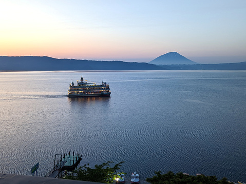 Toyako-cho, Japan - June 8, 2023: Espoir, the floating castle, cruises Toyako, a caldera lake. Mount Yotei stands in the distance. Spring twilight in Shikotsu-Toya National Park, Abuta District.