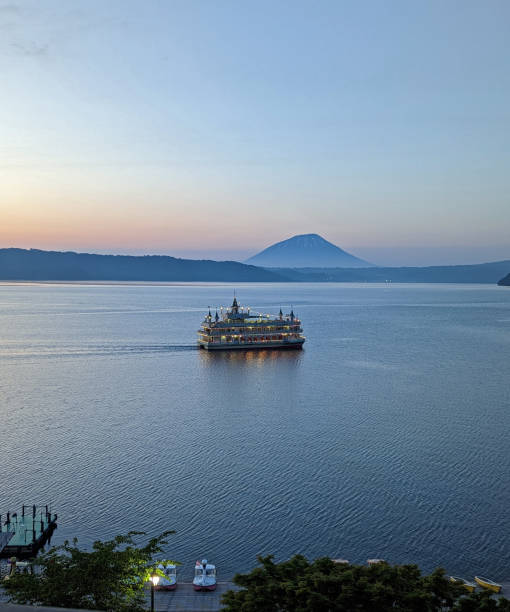 Toyako-cho, Japan - June 8, 2023: Espoir, a sightseeing cruiser, shows visitors the caldera lake of Toyako. Mount Yotei, a stratovolcano, stands in the background. The south lakeshore includes recreational boat rentals. Springtime in Hokkaido Prefecture.