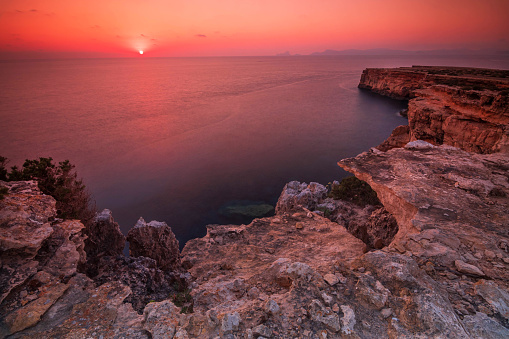 Sunset in balearic island of Formentera, on the west coast cliffs with Ibiza island on the horizon, with the sun above the sea.