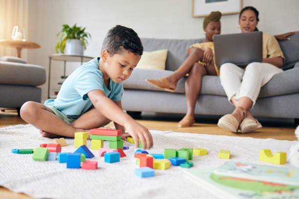 istock Play, toys and child on floor with parents on sofa for learning, development and education. Lgbtq family, home and boy with building blocks for fun, relax and games with lesbian mothers on laptop 1621516740