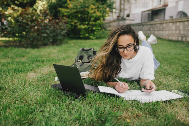 istock Young woman student studying using her books, laptop and notebook, sitting on grass. 1621520561
