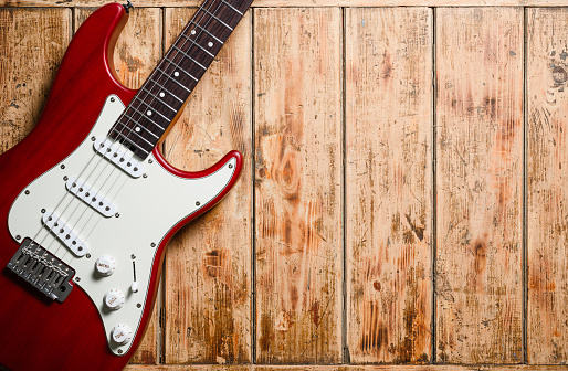 Red electric guitar on a wooden background. Empty space, close-up.