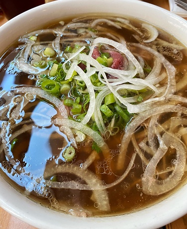 A bowl of beef pho soup with onions, cilantro, and noodles