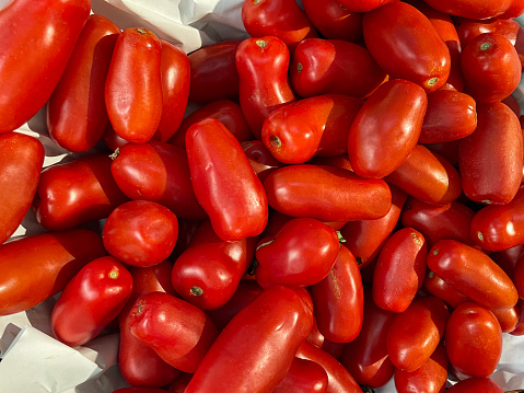 Stock photo showing close-up, elevated view of pile of glossy plum tomatoes on stall for sale at a fruit and vegetable market.