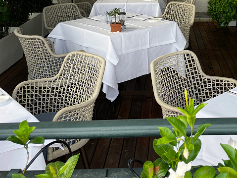 Stock photo showing close-up view of restaurant al fresco wood deck area with tablecloth covered tables under an awning.