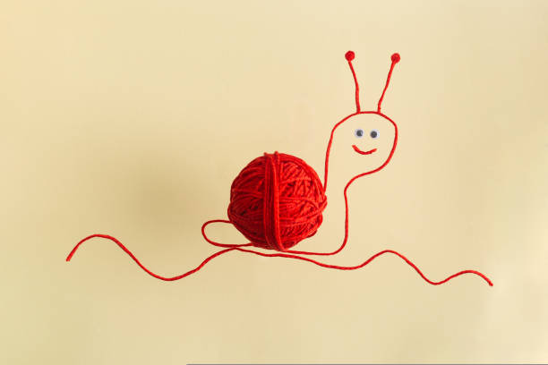 Drawing of red snail from wool threads with ball integrated knitting creative concept flat lay on beige. High quality photo