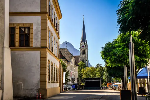 View Of Street Leading To St. Florin Cathedral With It's Mighty Clocktower In Vaduz, Liechtenstein
