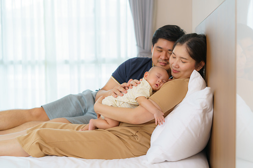 Asian father and mother holding their infant son in the bedroom at home, representing love and family bonds.