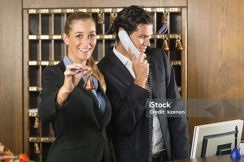 Reception in hotel - Man and woman Reception in hotel - Man and woman standing at the front desk, man taking a call, woman holding a key in the hand and smiling Hotel Reception Stock Photo
