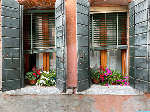 Stock photo showing close-up view of colourful orange house exterior in Burano, Venice, Italy with two wood framed casement windows with wooden shutters and Venetian blinds. Famous for lace making, Burano is an island in the Venetian Lagoon.
