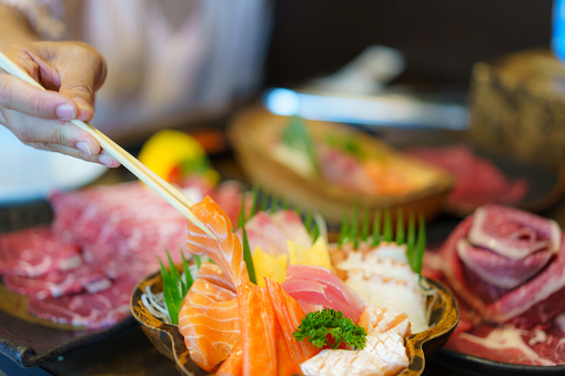 A woman hand wields chopsticks to delicately place fresh salmon sashimi on a plate in a Japanese restaurant, capturing the art of dining.