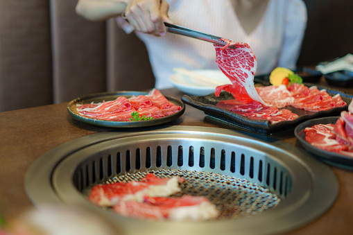 woman's hand employs tongs to place wagyu beef on a plate, ready to grill over charcoal, enhancing the dining experience at a Japanese restaurant
