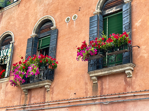 Stock photo showing close-up view of colourful orange house exterior in Burano, Venice, Italy with a Juliet balconies outside a sash windows with wooden shutters and Venetian blinds. Famous for lace making, Burano is an island in the Venetian Lagoon.