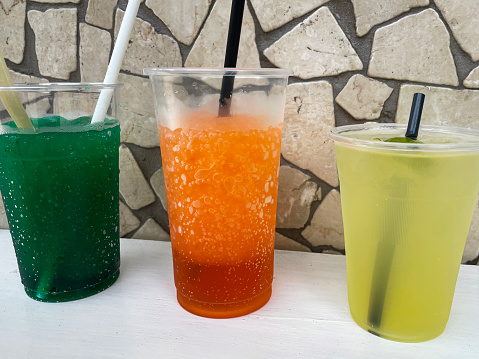 Stock photo showing a mosaic, crazy paving styled wall behind a table containing a row of vibrant coloured ice cold drinks.