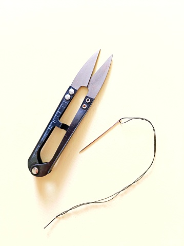 istock A black scissor and a needle with black thread isolated on cream colour background 1621724150