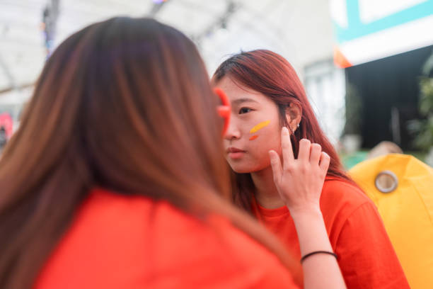 tifoso di calcio che mette la vernice per il viso mentre si prepara per la partita. - stage makeup make up women body paint foto e immagini stock