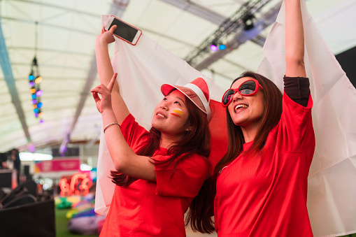 Two female friends holding national flag of a country enjoying, watching a soccer match.