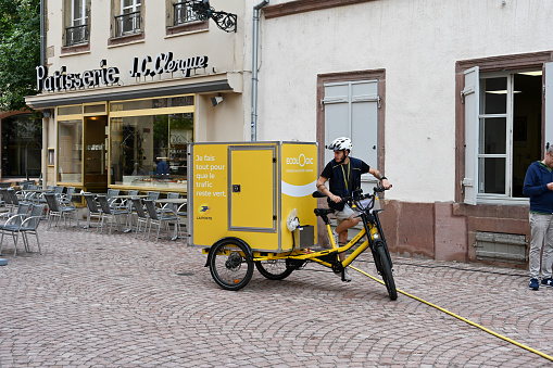 Colmar, France, July 25, 2023 - French Post Office (la Poste) letter carrier delivering mail in the historic old town of Colma on an electric bicycle.