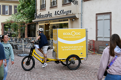 Colmar, France, July 25, 2023 - French Post Office (la Poste) letter carrier delivering mail in the historic old town of Colma on an electric bicycle.