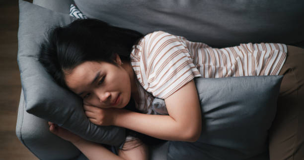 istock Pensive depressed young Asian woman lying on sofa at home looking at ceiling thinking pondering 1621993680