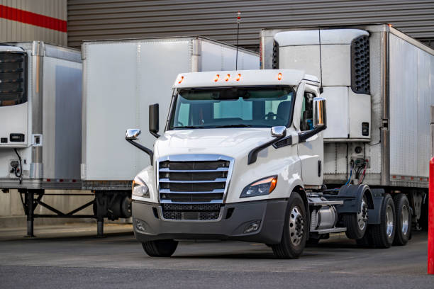 istock Day cab white big rig semi truck tractor with refrigerator semi trailer unloading delivered cargo parking in store dock gate beside the another unloading trailers 1621993954