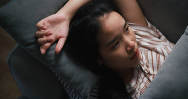 istock Pensive depressed young Asian woman lying on sofa at home looking at ceiling thinking pondering 1621995596