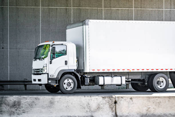 istock Compact small rig cab over semi truck with long box trailer transporting cargo running on the road under the bridge 1621996643